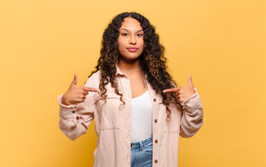 young hispanic woman looking proud, positive and casual pointing to chest with both hands