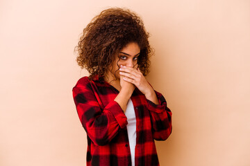 Young african american woman isolated on beige background covering mouth with hands looking worried.