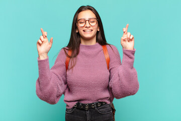 Wall Mural - young pretty woman smiling and anxiously crossing both fingers, feeling worried and wishing or hoping for good luck. student concept