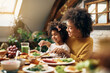 © Drazen - Happy African American mother and daughter eating at dining table.