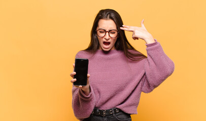 Wall Mural - young pretty woman looking unhappy and stressed, suicide gesture making gun sign with hand, pointing to head. phone screen concept