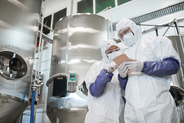 low angle view at two workers wearing protective suits while using digital tablet at modern chemical