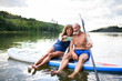 © Halfpoint - Senior couple sitting on paddleboard on lake in summer, taking selfie with smartphone.