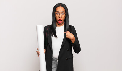 Wall Mural - young black woman looking shocked and surprised with mouth wide open, pointing to self. architect concept