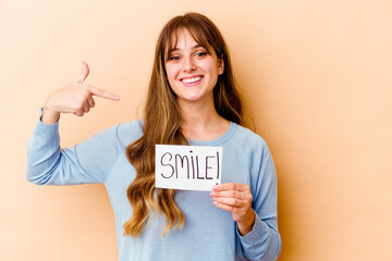 Wall Mural - Young caucasian woman holding a Smile placard isolated person pointing by hand to a shirt copy space, proud and confident