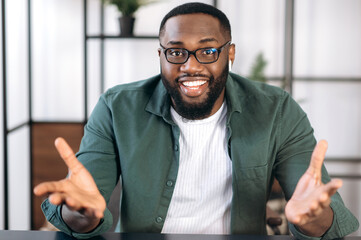 Wall Mural - Successful friendly multiracial black male freelancer, business leader or tutor, speaking during video conference with colleagues or friends, gesturing hands and smiling, talks about plans,strategy