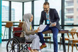© KPs Photography  - The manager is using the tablet while he is listening the female employee present the information of the report. Female muslim officer is sitting on the wheelchair and holding the document on hand.