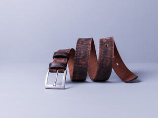 The belt is made of genuine brown leather with a worn texture. Wooden background painted with gray paint.