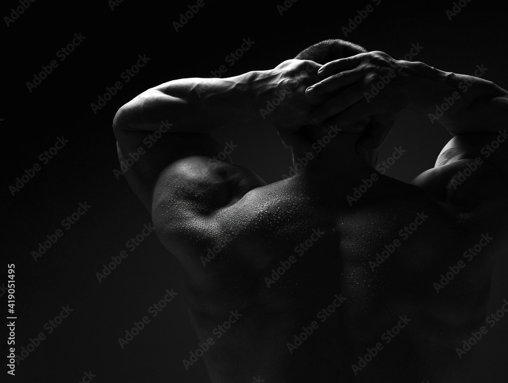 Strong muscular man, athlete, sportsman is standing naked, shirtless with his back to camera holding hands behind head over dark background - obrazy, fototapety, plakaty 