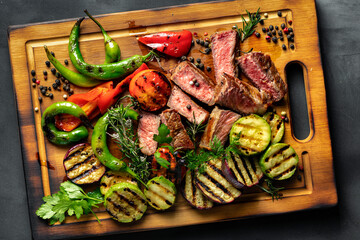 Wall Mural - Sliced fried medium steak with grilled vegetables on a wooden cutting board top view