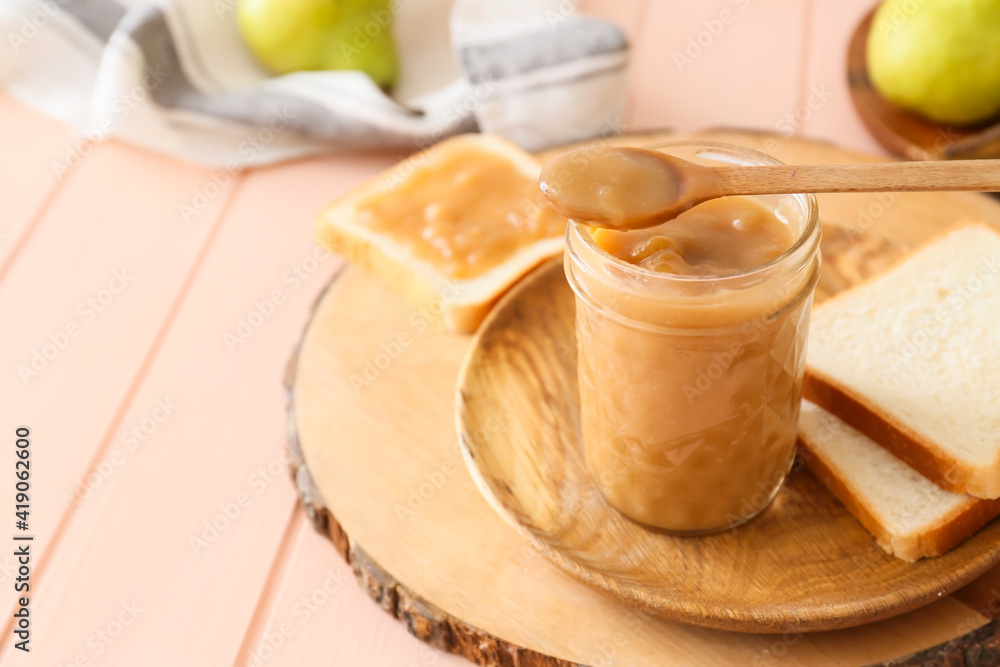 Jar of tasty pear jam with bread on wooden table