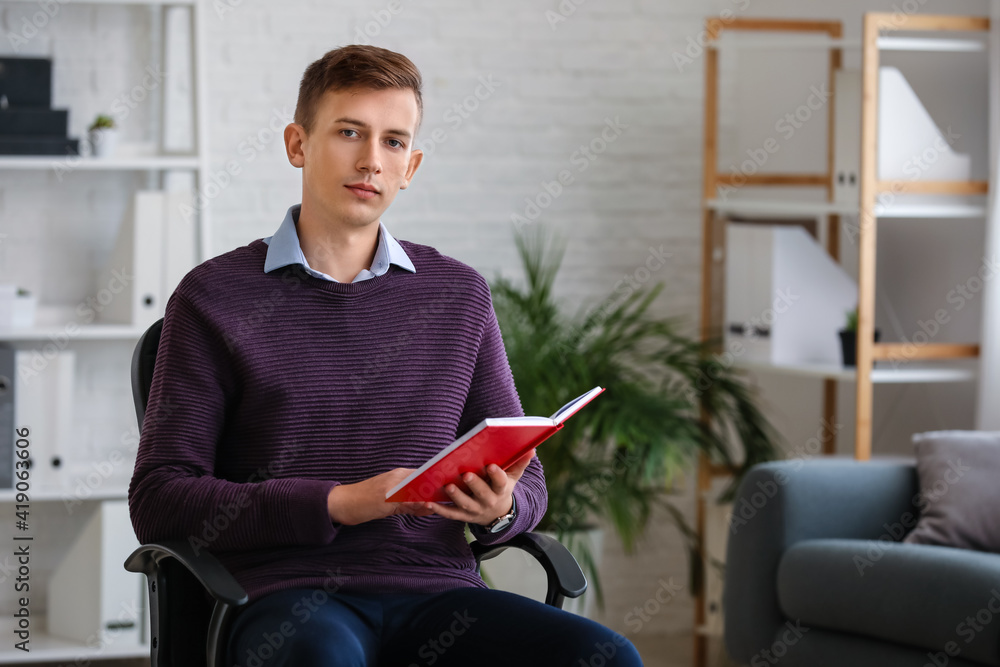 Young man reading red book in office