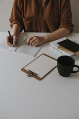 Wall Mural - Woman write in a blank sheet notebook. Minimalist home office desk workspace with coffee cup, clipboard. Work, business background.
