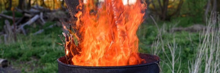 garbage incineration in rusty metal barrel. burning branches and old grass from the land plot. spring cleaning of the backyard and garden. a safe alternative to spring grass burn. banner