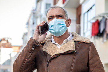 Wall Mural - mature man with medical mask talking on the mobile phone in prevention against viruses and diseases