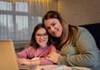 Mother and daughter follow online classes using laptop at home.