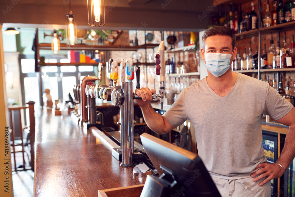 Portrait Of Male Bar Worker Wearing Face Mask During Health Pandemic Standing Behind Counter - obrazy, fototapety, plakaty 