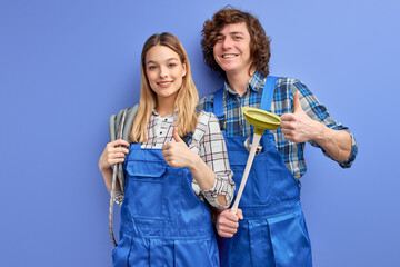 cheerful man and woman plumbers in blue uniform with plunger tool, being glad to repair bathtub for clients, recieve pleasant comments from clients, isolated over blue studio background