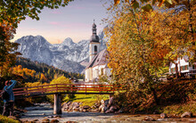 Wonderful Sunny Autumn Landscape In Bavarian Alps. Incredible View Of Famous St. Sebastian Parish Church. Amazing Nature Scenery With Mountains, Colorful Trees And River. Popular Travel Destination.