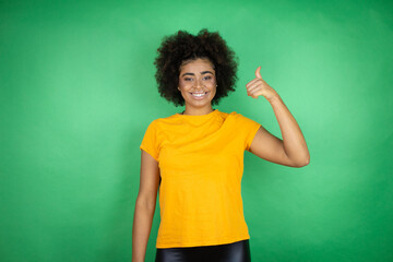 African american woman wearing orange casual shirt over green background success sign doing positive gesture with hand, thumb up smiling and happy. cheerful expression and winner gesture.