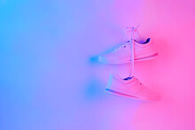 Pair Of Stylish Sneakers Hanging On Wall. White Shoe Isolated On Neon Background.