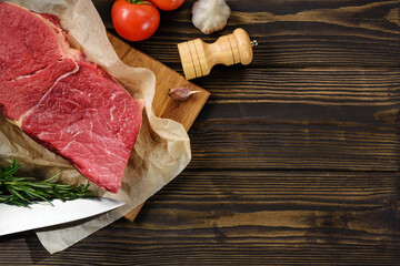 A piece of fresh beef, a tomato knife and seasoning on a wooden table with a copy space.