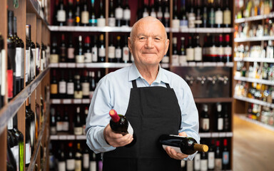 Happy senior male vintner giving recommendation about purchase wine in his wine house