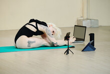 Fit Young Woman Sitting On Floor And Leaning Forward To Her Legs When Filming Stretching Workout