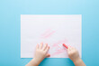 © fotoduets - Baby hand holding red wax crayons and drawing first scratches lines on white paper on light blue table background. Pastel color. Closeup. Toddler development. Point of view shot. Top down view.