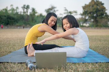 Wall Mural - Mother and daughter doing yoga. woman and child training in the park. outdoor sports. healthy sport lifestyle,watching yoga exercises online video tutorial and seated forward bend pose.