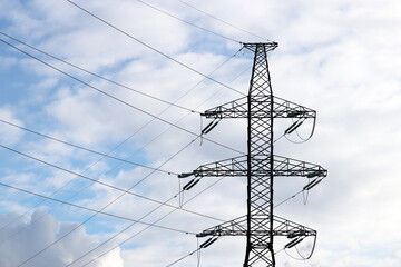 High voltage tower with electrical wires on blue sky with white clouds. Electricity transmission lines, power supply concept