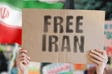 The Phrase " Free Iran " On A Banner In Men's Hand With Blurred Iranian Flag On The Background. Protest. Riot. Violence. Economic Crisis. Collapse. Politics. Streets. Save. Cruelty