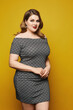 A young plump woman in a short grey dress poses over a yellow background, isolated