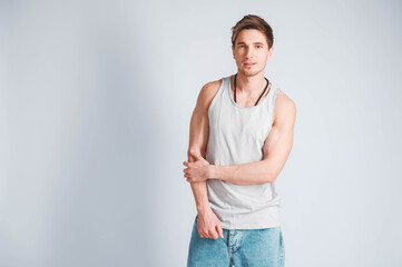 Wall Mural - Young muscular man in a light T-shirt and jeans on a white background. Copy, empty space for text