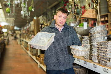 Wall Mural - Puzzled man choosing handmade wickerwork for interior in home decor shop..