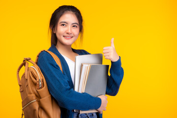 Happy college young girl student smiling at camera on yellow background with thumb up holding tablet and lecture books, hanging bag pack. Youth girl student look clever and smart. education concept