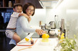 Vietnamese woman giving piggyback ride to her kid when cooking breakfast for family and making fresh orange juice
