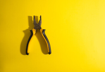 The old yellow-black pliers on the yellow background with traces of dirt