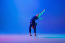 Energy. Young Flexible Girl Isolated On Blue Studio Background In Neon Light. Young Female Model Practicing Artistic Gymnastics. Exercises For Flexibility, Balance. Grace In Motion, Sport, Action.