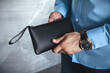 A business man in the interior holds a leather black clutch in his hands. No face, horizontal orientation