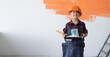 © Andrii Lysenko - a boy dressed in overalls stands in the room holding a can of paint in his hands. Home renovation concept.
