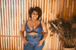 © Алина Троева - Beautiful stylish curvy oversize African black woman with afro hair posing in bra and jeans on wooden eco friendly background, body imperfection, body acceptance, body positive and diversity concept..