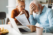 © Goran - Frustrated senior couple sitting at home and checking their home finances