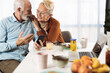 © Goran - Happy mature couple text messaging on their cell phone at home