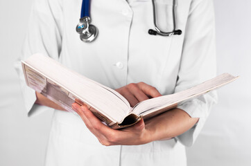 Doctor or medical student in uniform reading thick book on medicine, prepare for exam with textbook