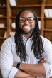 © Vadim Pastuh - Vertical close-up portrait of cheerful African-American businessman wearing stylish eyeglasses with dreadlocks, a guy stands with arms crossed and looking at camera with a friendly toothy smile