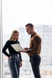 © DSMT - A successful female office worker with a colleague with a netbook stands in a skyscraper against the backdrop of a window overlooking the city. City architects looking at laptop happy with project