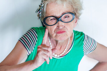 Stylish emotional elderly woman with an evil face waving index finger over white background. Concept protest and objection of an old woman. Morality and censure. Grumpy grandmother. Angry woman