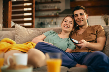 Wall Mural - Happy couple watching movie while relaxing on the sofa at home.