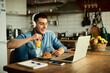 © Drazen - Smiling man with headphones surfing the net on laptop while working at home.